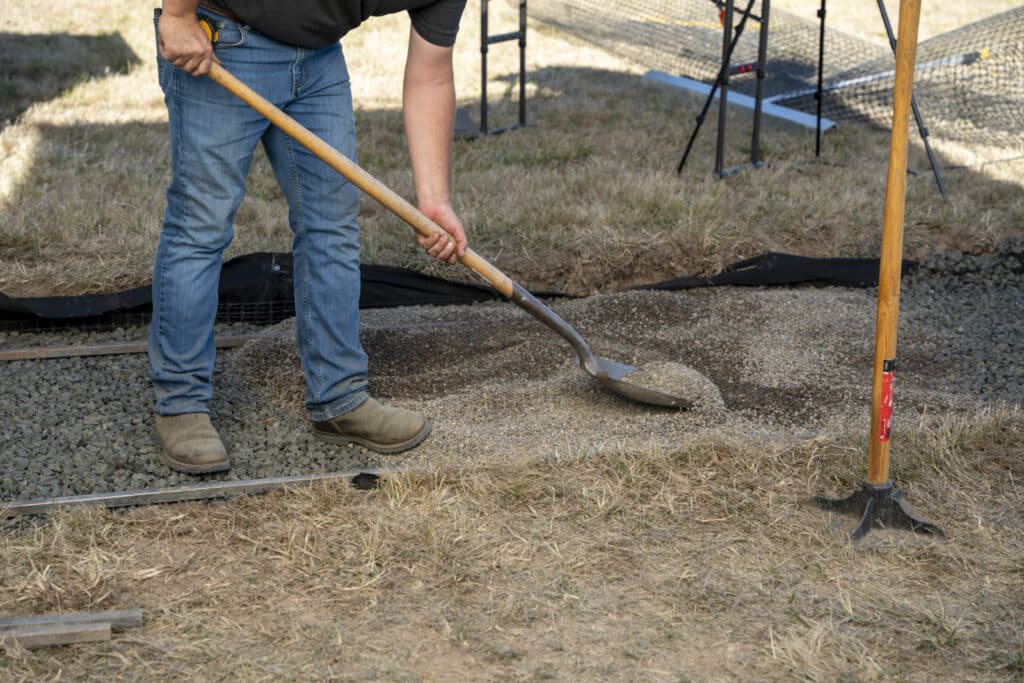 Using a shovel and hand tamper as essential tools for paver base preparation.